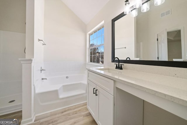 bathroom featuring a garden tub, lofted ceiling, visible vents, vanity, and wood finished floors