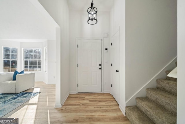 foyer entrance featuring light wood finished floors, baseboards, a high ceiling, and stairway