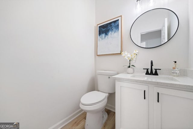 half bathroom featuring toilet, baseboards, wood finished floors, and vanity