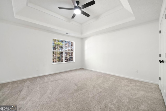 empty room with a raised ceiling, light colored carpet, and baseboards