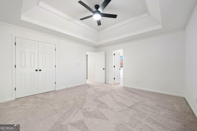 unfurnished bedroom with light carpet, baseboards, a raised ceiling, ceiling fan, and a closet