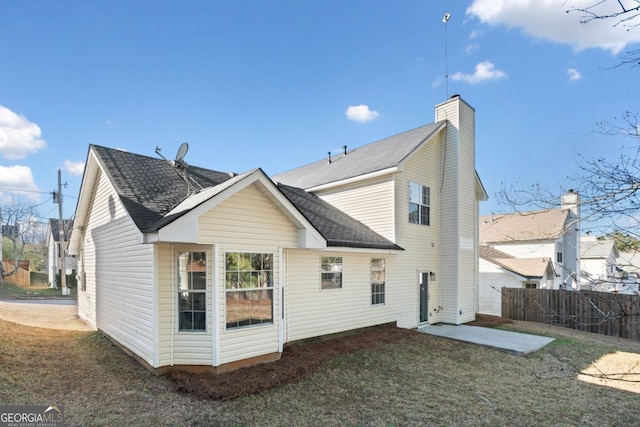 rear view of house featuring a patio, fence, a yard, roof with shingles, and a chimney