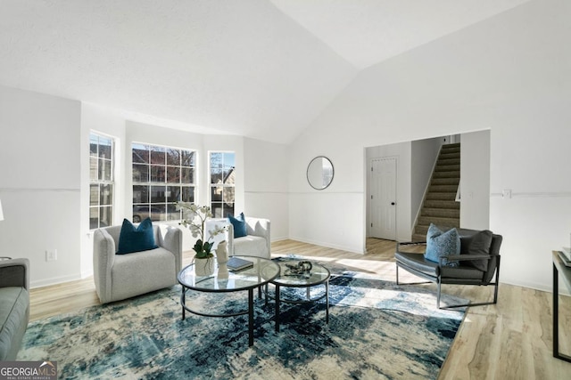 living room with light wood finished floors, baseboards, stairway, and high vaulted ceiling