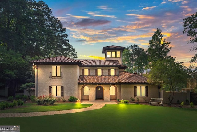 mediterranean / spanish-style house featuring a yard, fence, a tiled roof, and stucco siding