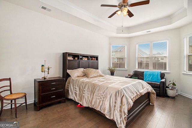 bedroom featuring a tray ceiling, dark wood-type flooring, visible vents, and baseboards