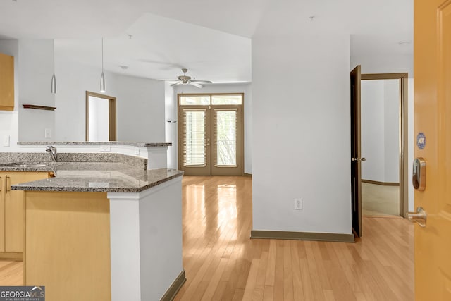 kitchen with french doors, light wood-style flooring, ceiling fan, a sink, and dark stone counters