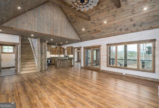 unfurnished living room featuring high vaulted ceiling, light wood finished floors, stairway, and plenty of natural light