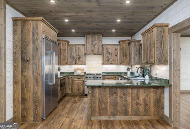 kitchen with a peninsula, dark wood-type flooring, a sink, high quality appliances, and custom range hood