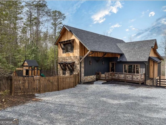 view of front facade featuring stone siding, roof with shingles, fence, and a deck