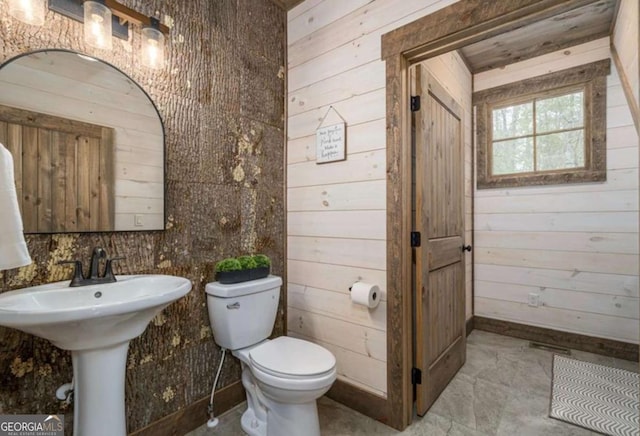 half bath with toilet, wood walls, and a sink