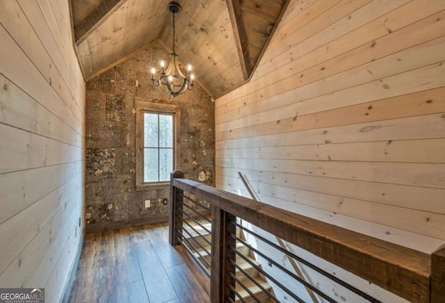 hallway featuring wooden walls, wood finished floors, vaulted ceiling with beams, an inviting chandelier, and an upstairs landing