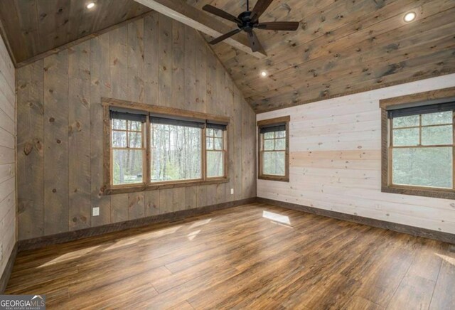 empty room featuring a wealth of natural light, ceiling fan, wooden walls, and wood finished floors