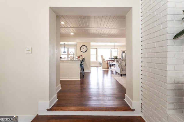 hallway featuring dark wood-style flooring, brick wall, and baseboards