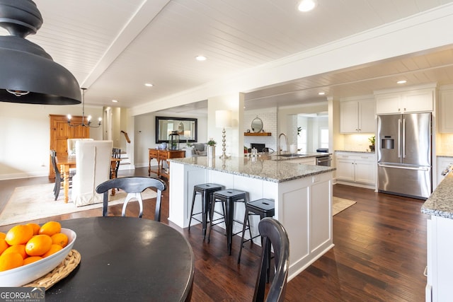 kitchen featuring stainless steel fridge with ice dispenser, dark wood-style floors, light stone counters, white cabinetry, and a sink