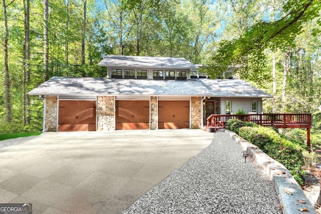 mid-century modern home featuring driveway, stone siding, an attached garage, and a deck