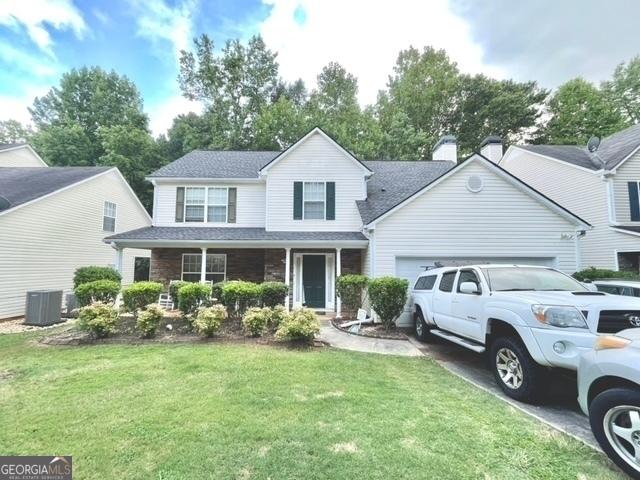 traditional home with a garage, a porch, a front yard, and central air condition unit