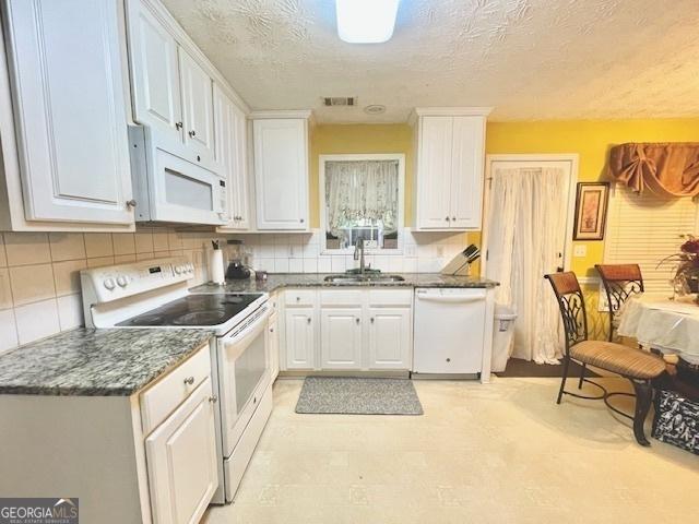 kitchen with white appliances, visible vents, white cabinetry, and a sink