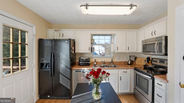 kitchen featuring white cabinets, appliances with stainless steel finishes, light countertops, light wood-style floors, and a sink