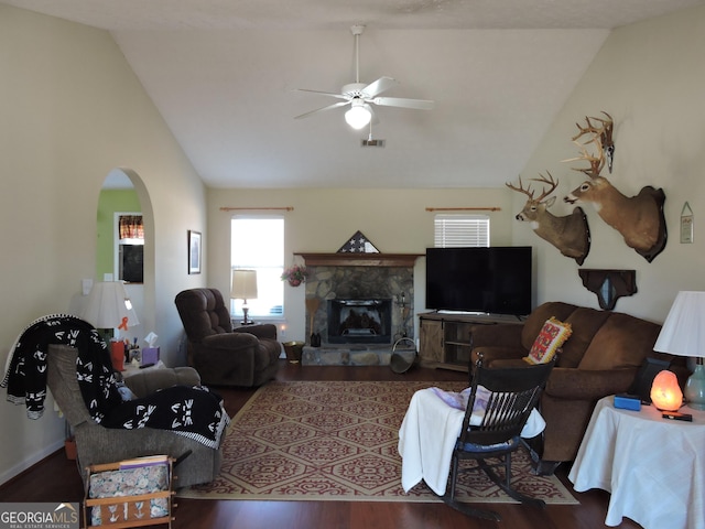 living room with arched walkways, dark wood-style flooring, a fireplace, visible vents, and a ceiling fan