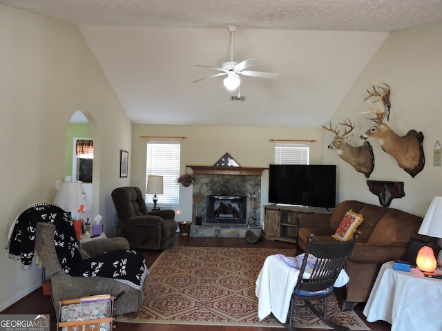 living area featuring arched walkways, a fireplace, visible vents, ceiling fan, and wood finished floors