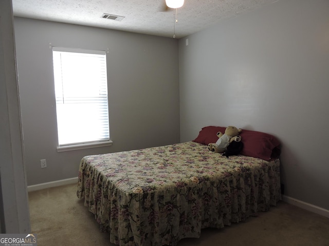 bedroom with visible vents, light colored carpet, a textured ceiling, and baseboards