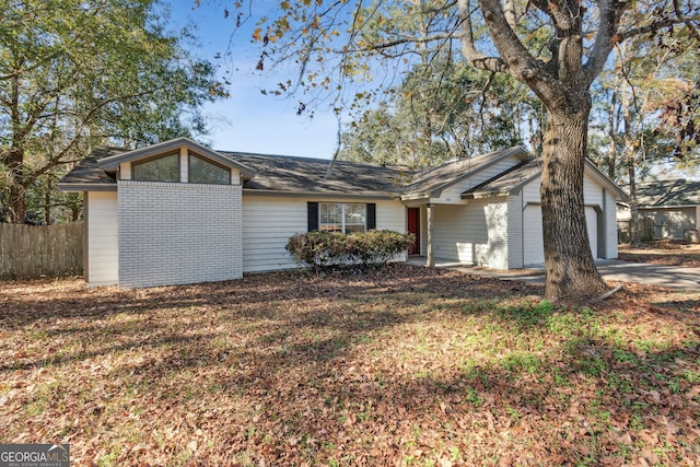 view of front facade featuring brick siding, driveway, an attached garage, and fence