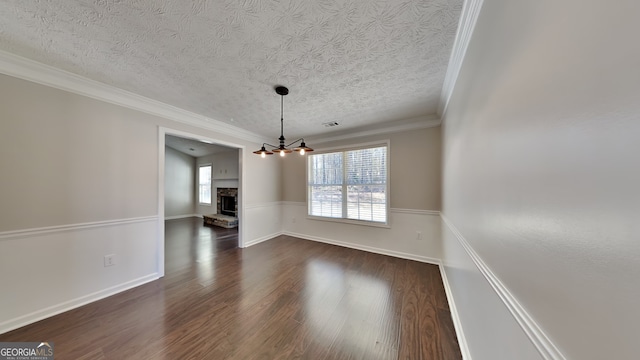 unfurnished dining area with a fireplace, dark wood finished floors, ornamental molding, a textured ceiling, and a chandelier