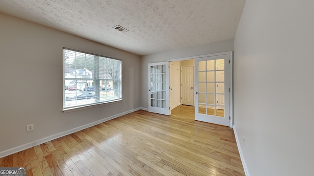 spare room featuring french doors, visible vents, light wood-style flooring, a textured ceiling, and baseboards