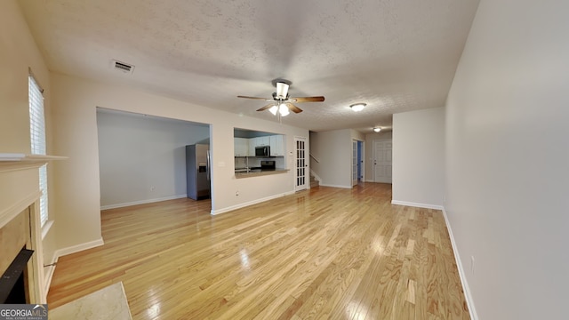 unfurnished living room with visible vents, stairway, a textured ceiling, light wood-style floors, and a fireplace