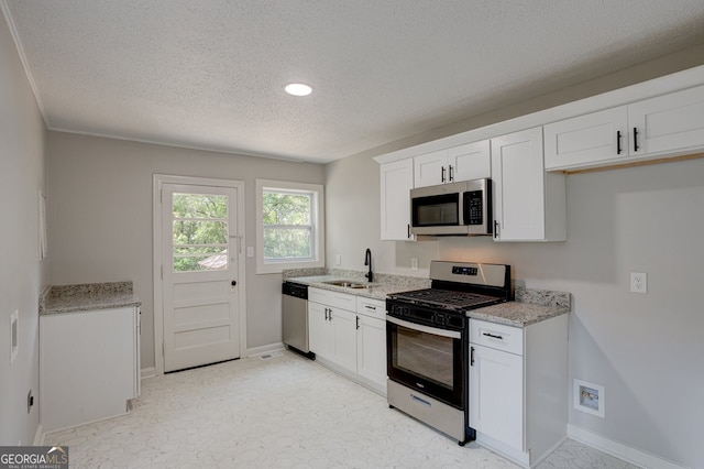 kitchen featuring appliances with stainless steel finishes, white cabinets, a sink, and light stone counters