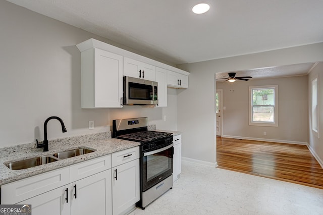 kitchen featuring baseboards, light stone countertops, stainless steel appliances, white cabinetry, and a sink