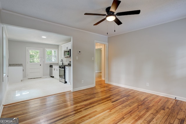 unfurnished living room with light wood finished floors, baseboards, a ceiling fan, ornamental molding, and a textured ceiling