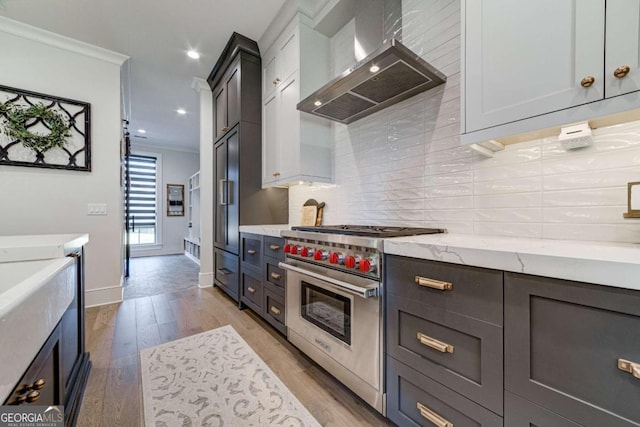 kitchen featuring crown molding, light wood-type flooring, wall chimney range hood, backsplash, and luxury stove