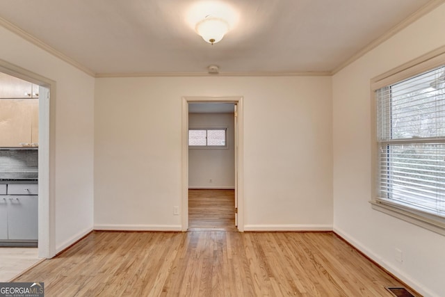 spare room featuring light wood-style floors, baseboards, visible vents, and crown molding