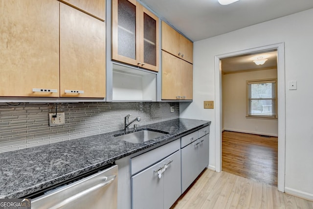 kitchen with a sink, stainless steel dishwasher, backsplash, dark stone counters, and glass insert cabinets