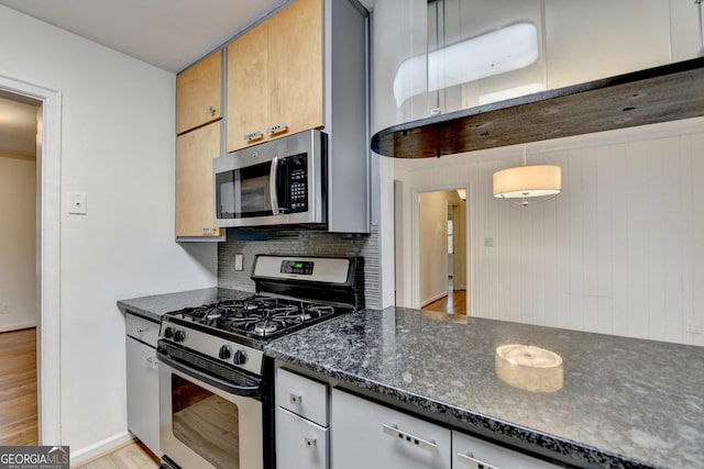 kitchen with light wood finished floors, dark stone counters, decorative backsplash, brown cabinetry, and stainless steel appliances