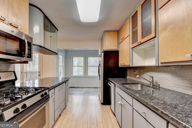 kitchen featuring stainless steel appliances, tasteful backsplash, glass insert cabinets, a sink, and dark stone countertops