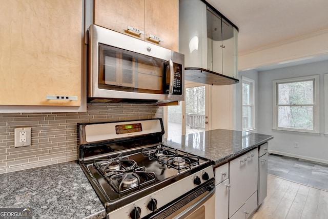 kitchen featuring stainless steel appliances, baseboards, ornamental molding, backsplash, and dark stone countertops