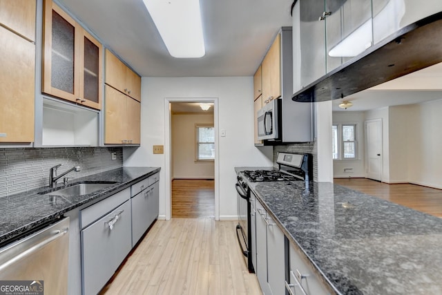 kitchen with stainless steel appliances, a sink, tasteful backsplash, dark stone countertops, and glass insert cabinets