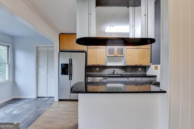 kitchen with backsplash, appliances with stainless steel finishes, dark stone counters, a sink, and light wood-type flooring