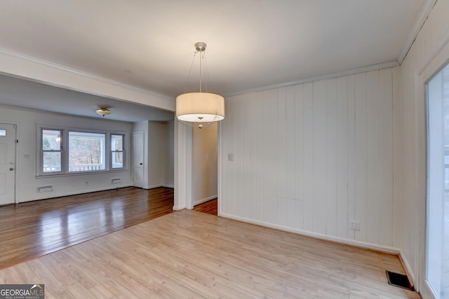 empty room with light wood-type flooring, baseboards, visible vents, and ornamental molding