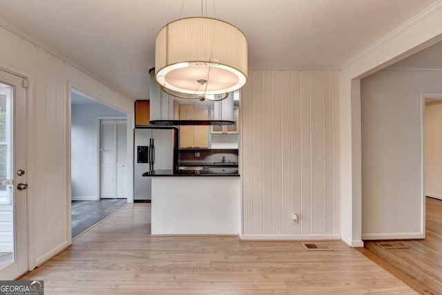 kitchen featuring visible vents, light wood-style floors, dark countertops, stainless steel fridge, and crown molding