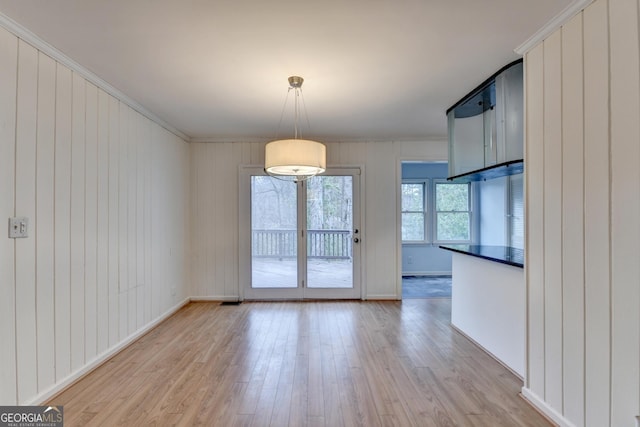 unfurnished dining area featuring baseboards, light wood finished floors, and crown molding