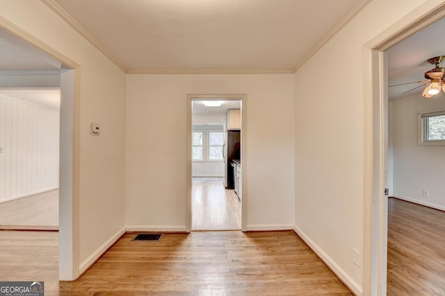 spare room featuring light wood finished floors, plenty of natural light, visible vents, and crown molding