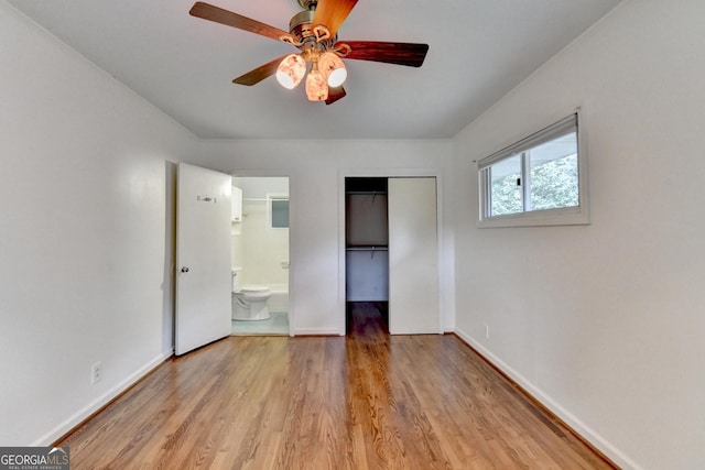 unfurnished bedroom featuring baseboards, light wood-style flooring, ceiling fan, ensuite bathroom, and a closet