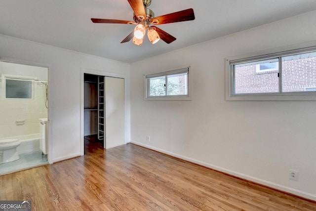 unfurnished bedroom featuring baseboards, ensuite bath, ceiling fan, light wood-style floors, and a closet