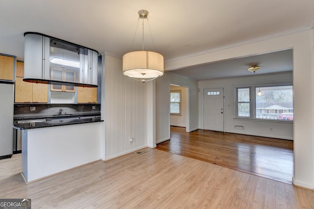 kitchen with a sink, light wood-type flooring, backsplash, freestanding refrigerator, and pendant lighting