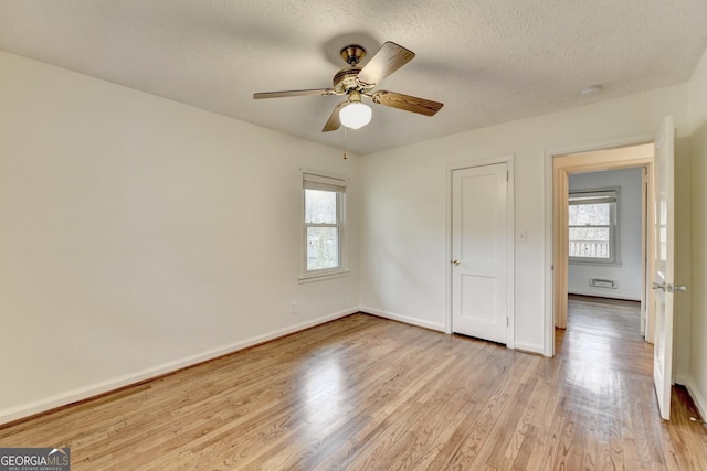 unfurnished bedroom featuring a textured ceiling, light wood finished floors, multiple windows, and baseboards