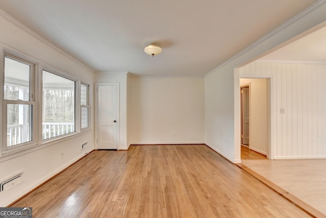 spare room featuring a baseboard heating unit, light wood-style flooring, ornamental molding, and baseboards