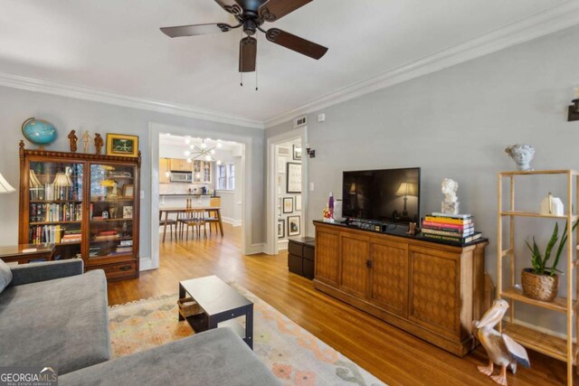 living room with ornamental molding, baseboards, light wood finished floors, and ceiling fan with notable chandelier